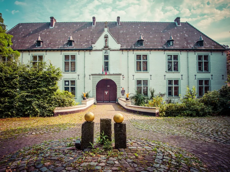 Voorgevel van Kasteel de Berckt met poort, ramen en geplaveide oprijlaan. Groen en gouden bollen sieren de entree. Perfecte locatie voor een rondleiding Kasteel de Berckt.
