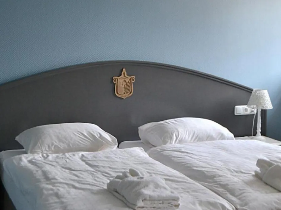 Doppelbett mit weißer Bettwäsche und Handtüchern, in einem gepflegten Hotelzimmer mit blauer Wand und klassischem Kopfteil.