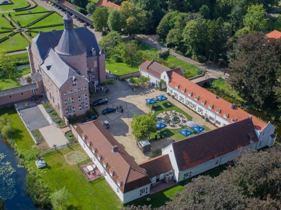 Luftaufnahme eines historischen Schlosses mit Innenhof, umgeben von Gebäuden mit roten Dächern und grünen Bäumen.