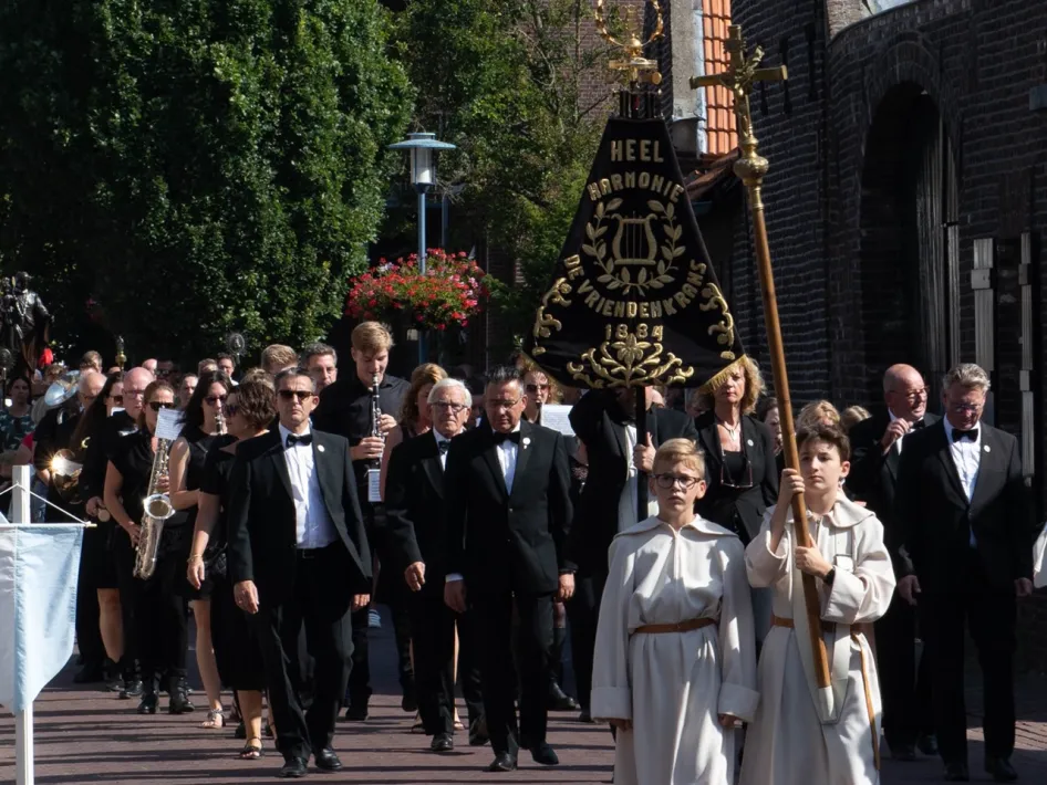 De kermisprocessie in Heel met harmonie De Vriendenkrans, kerkelijke vaandels en kinderen in witte gewaden.