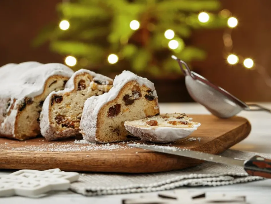 Plakjes kerststol op een houten plank tijdens de kerstbrunch bij Hotel Asteria Venray, met sfeervolle kerstverlichting op de achtergrond.