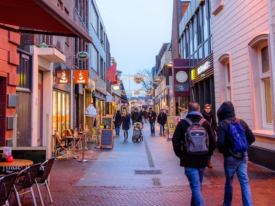 Mensen wandelen en winkelen in een sfeervol verlichte winkelstraat in het centrum tijdens koopzondag Weert.