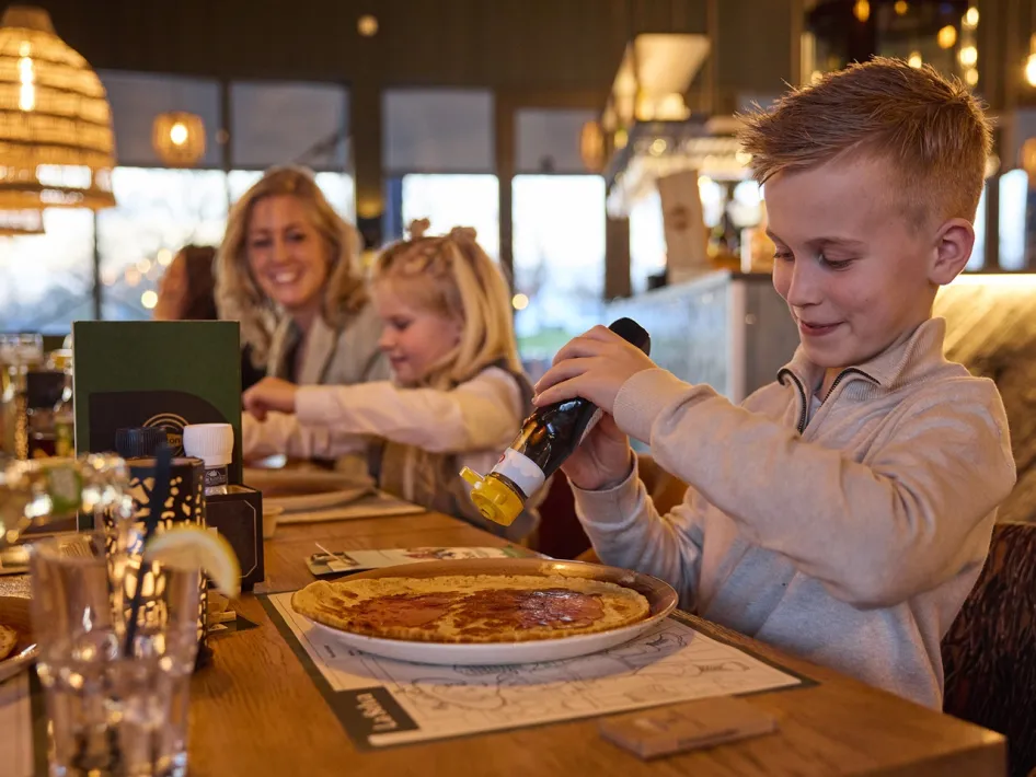 Ein Kind gibt Sirup auf einen Pfannkuchen am Tisch bei La Selva.