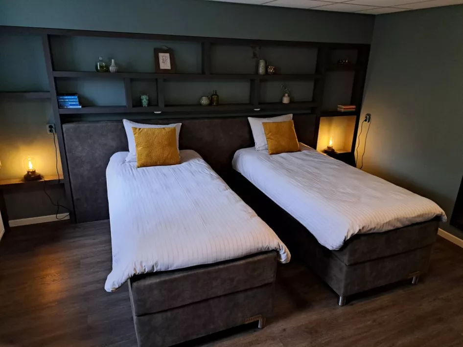 Sfeervolle tweepersoonskamer met twee boxspringbedden, gele sierkussens en warme verlichting.