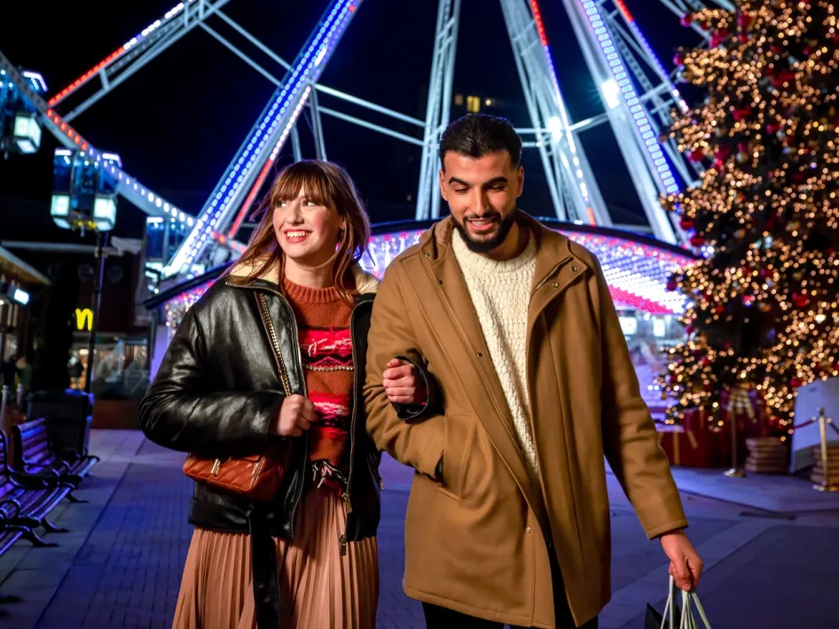 Jong stel loopt lachend door het sfeervol verlichte Designer Outlet Roermond tijdens het Last Minute XMAS Shopping.