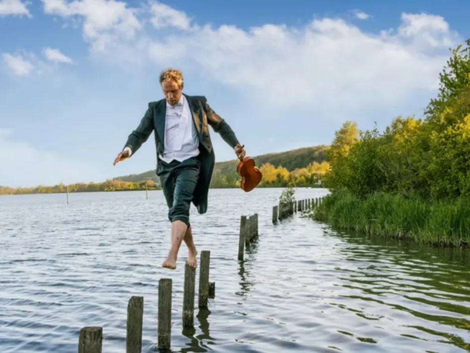 Muzikant balanceert met een viool over houten palen in het water tijdens Rondje Pontje Opera van het Limburg Festival.