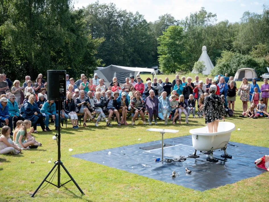 Publiek geniet van een openluchtvoorstelling tijdens Limburg Festival 2025, met een optreden in een badkuip op het gras.