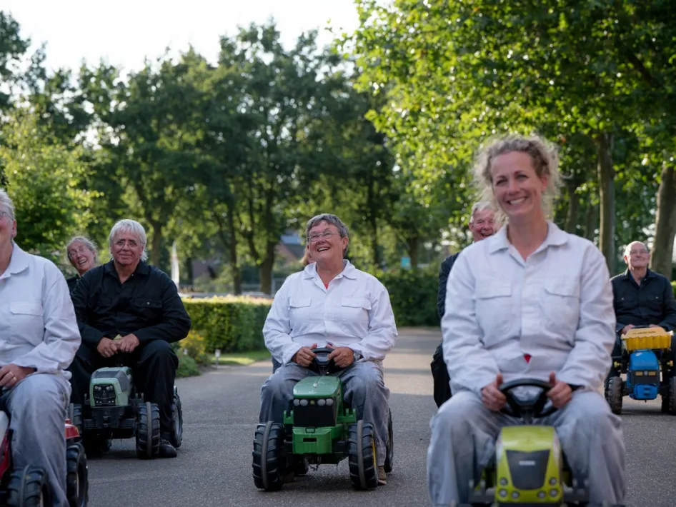 Deelnemers rijden lachend op speelgoedtractoren tijdens een humoristische voorstelling op Limburg Festival 2025.