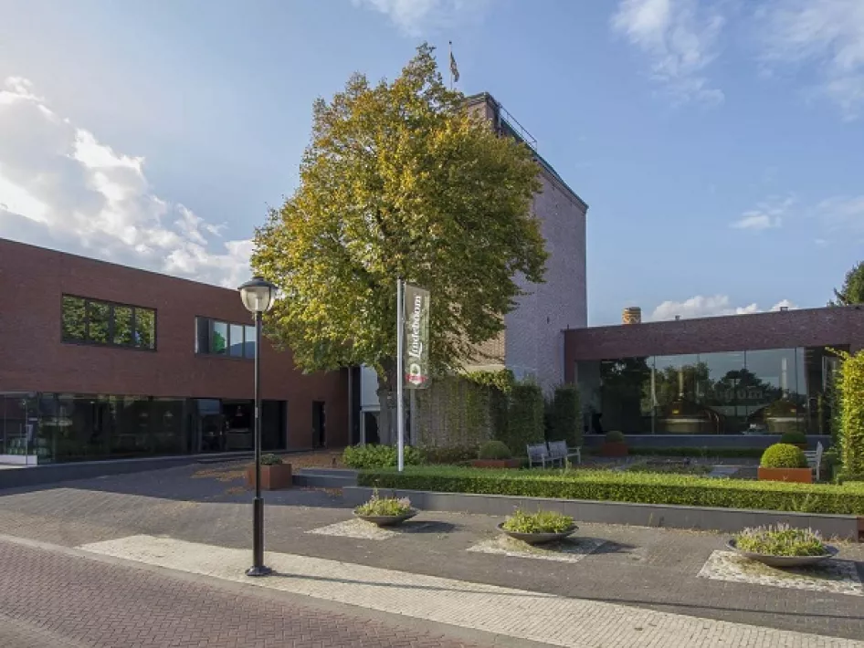 Modern brewery with red-brown facade, central tree and flagpole in front of the building in Neer.