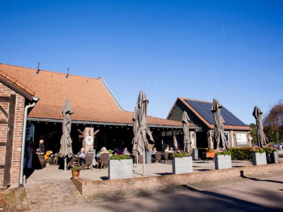 Terrace of Pannenkoekenhuis de Huifkarhoeve with parasols and seating by the brick farmhouse.