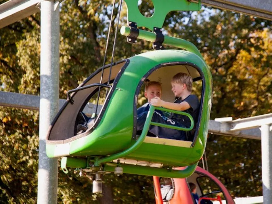 Kinder spielen in einem grünen Tret-Hubschrauber im Speeltuin de Gitstap