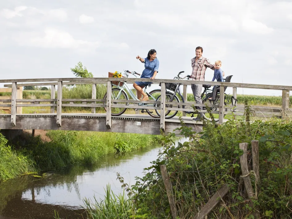 Gezin met fietsen pauzeert op een brug tijdens de route van Loeren bij de Boeren, met uitzicht op het Limburgse platteland.