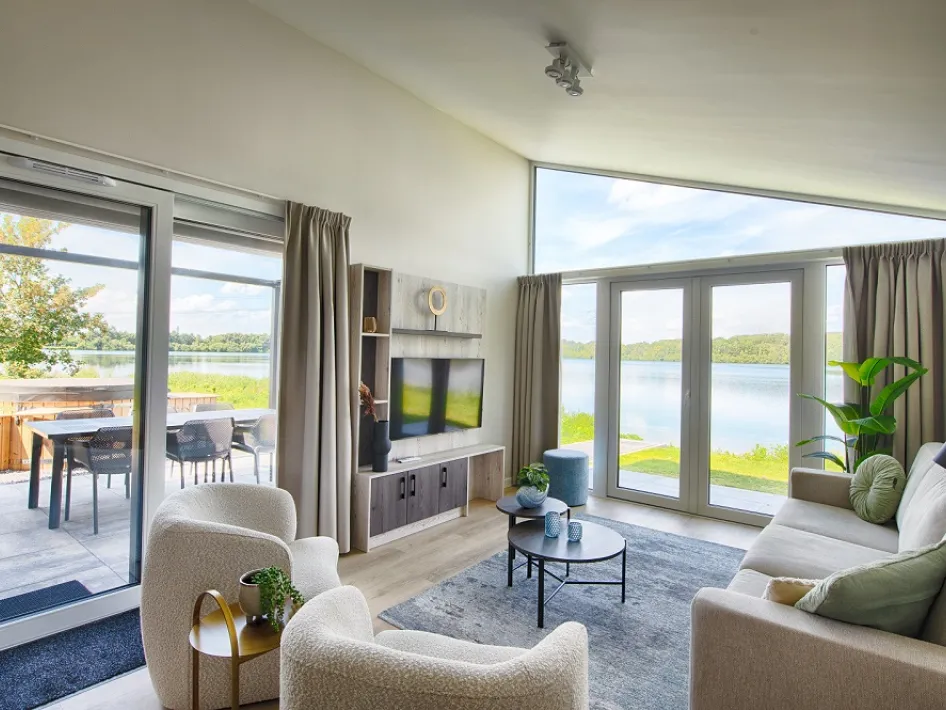 Een modern ingerichte woonkamer met grote ramen en een prachtig uitzicht op een meer en een buitenterras.