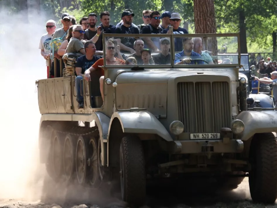 Een historische militaire halftrack met passagiers rijdt door een stoffig bos tijdens Militracks, een evenement met Tweede Wereldoorlog-voertuigen.