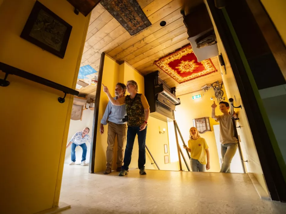 Een familie verkent een interactieve kamer in Mind Mystery, waarbij de scheve muren en plafonds een optische illusie creëren.