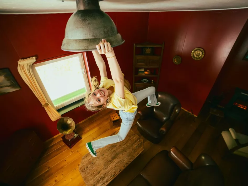 Ein Mädchen hängt lächelnd an einer Lampe in einem umgedrehten Raum, einem der interaktiven Erlebnisse bei Mind Mystery.