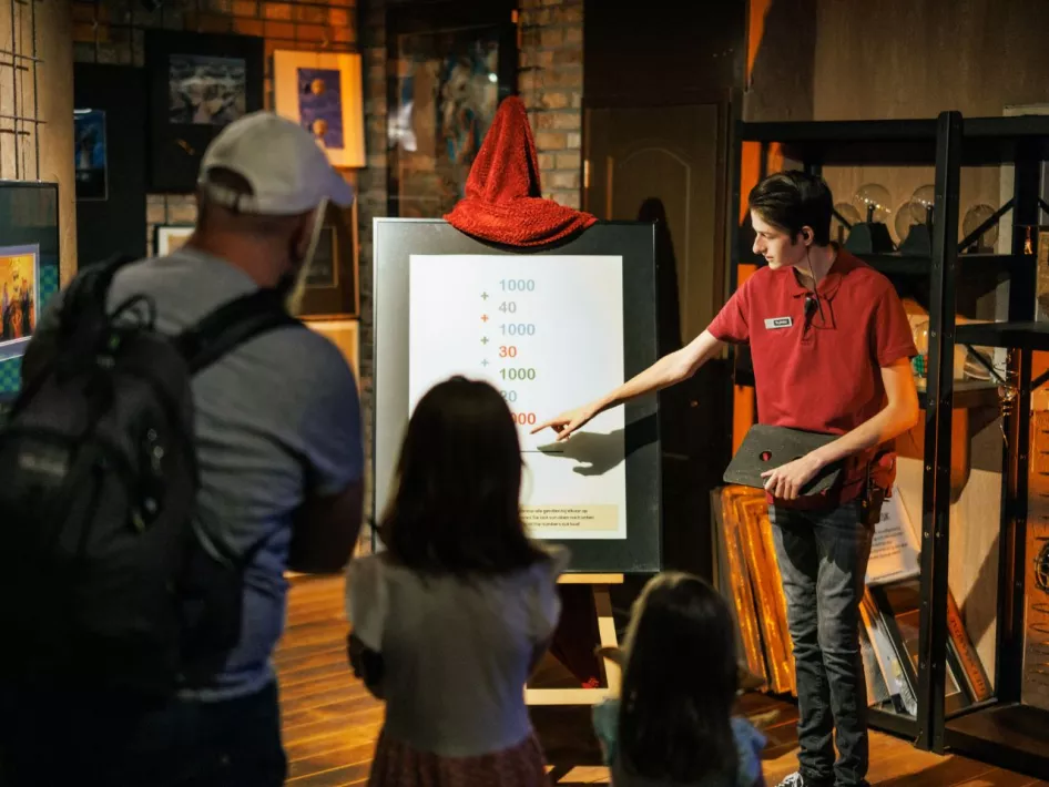 A guide at Mind Mystery explains to visitors, including children and adults, a visual puzzle on a board with numbers and colors.A guide at Mind Mystery explains to visitors, including children and adults, a visual puzzle on a board with numbers and colors.