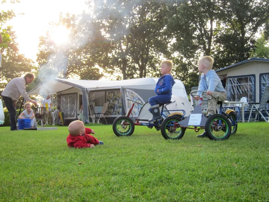 Kinderen zitten op hun fietsjes terwijl een baby op het trekkersvdeld ligt van Mini-camping de Linde