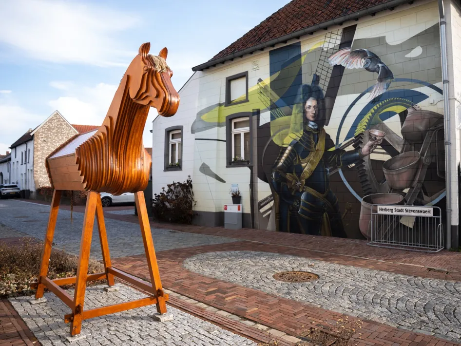 Wooden horse sculpture in Stevensweert in front of a wall mural of a miller