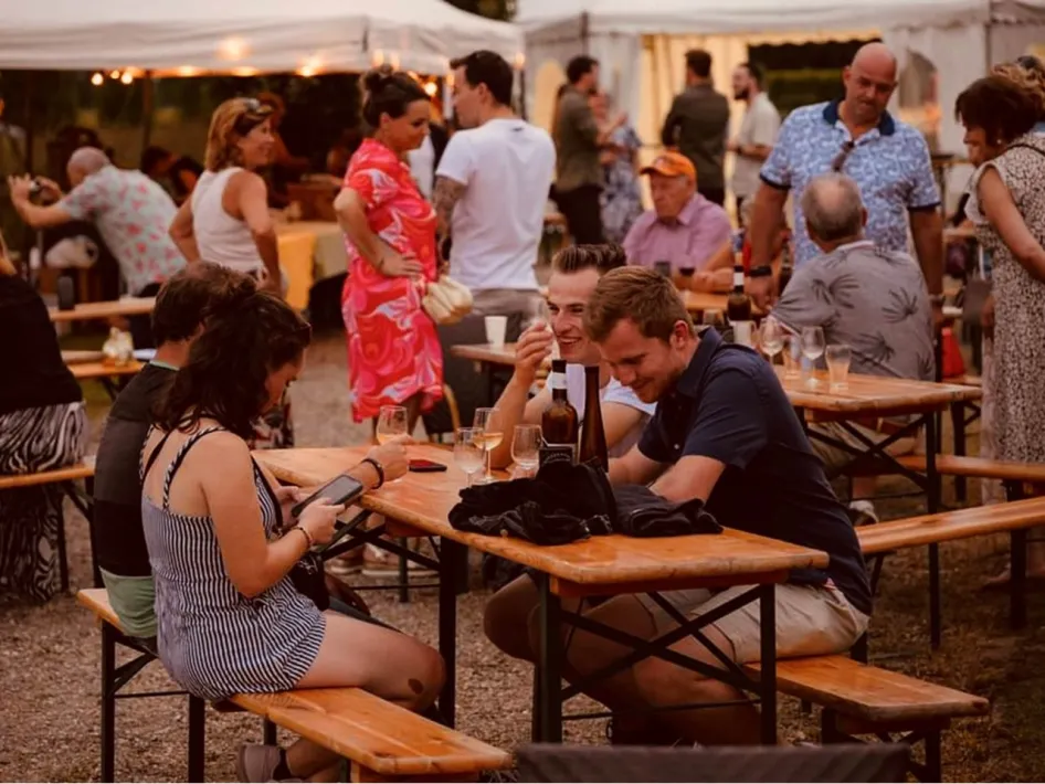 Gezellige drukte met bezoekers aan picknicktafels op het terrein van het Montforter Wijnfeest, met wijn, eten en muziek.