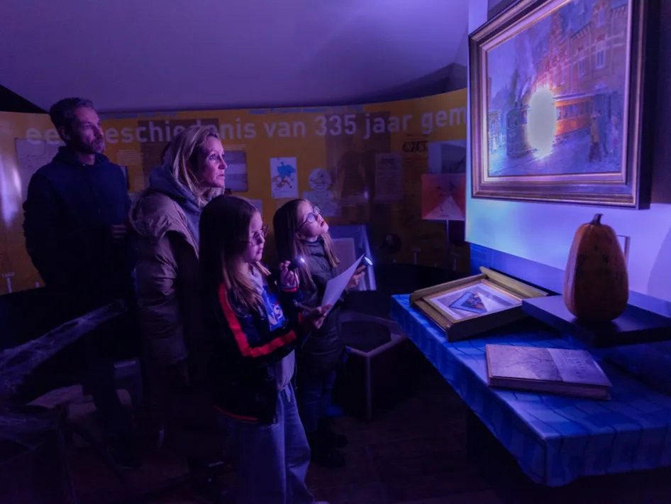 Bezoekers speuren met blacklightzaklampen naar verborgen aanwijzingen tijdens Museum in het Donker in Helden, terwijl een schilderij oplicht in het paarse licht.