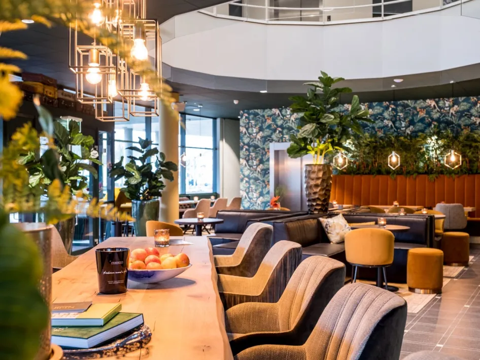 Stimmungsvolles Interieur des City Cafés im NERO Business Center & City Café mit bequemen Sitzplätzen, warmer Beleuchtung und viel Grün.