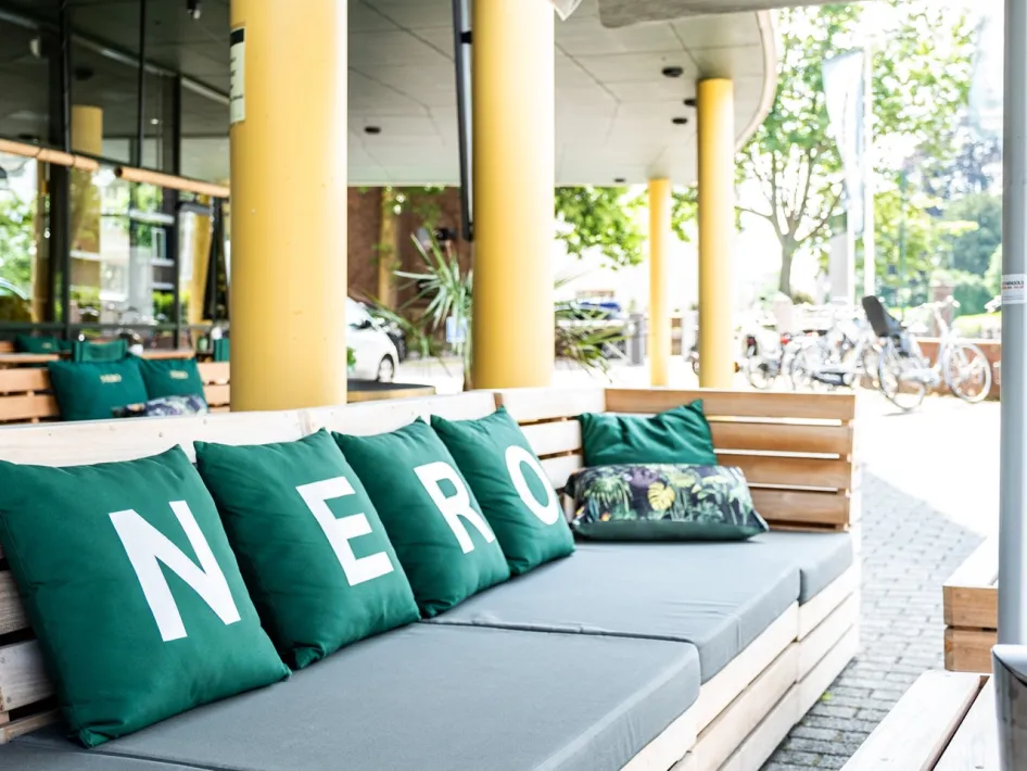 Lounge terrace at NERO Business Center & City Café with wooden benches and dark green cushions spelling out N-E-R-O.