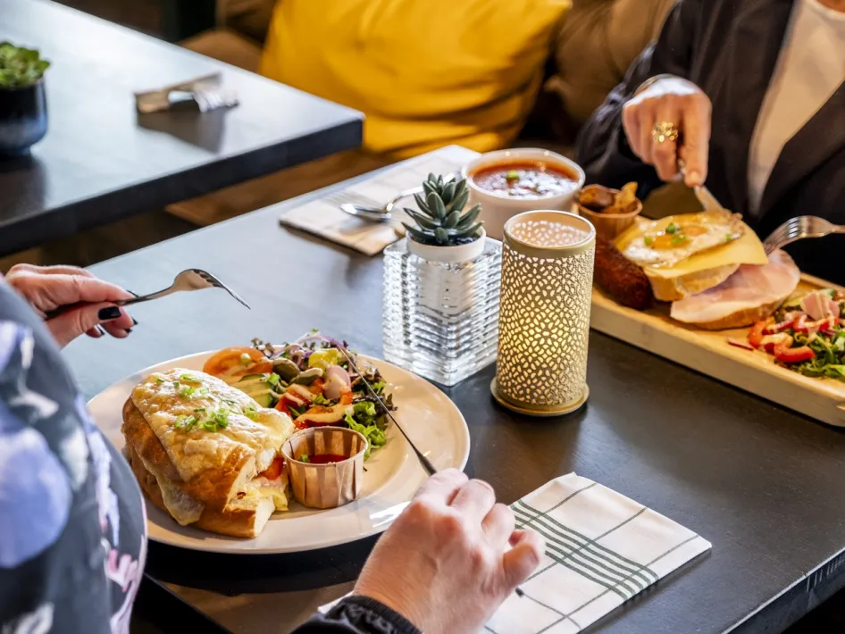 Zwei Personen genießen ein frisch zubereitetes Mittagessen mit Suppe, belegten Brötchen und Salat.