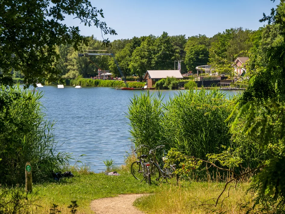 Two bikes stand at the De IJzeren Man recreational lake with the water ski track in the background