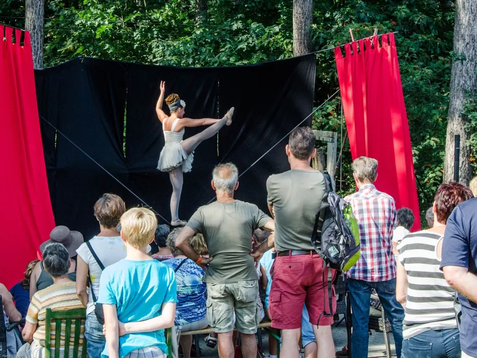Publiek kijkt naar een ballerina die optreedt op een klein openluchttheater tussen de bomen, tijdens een voorstelling van Natuurlijk… Theater.