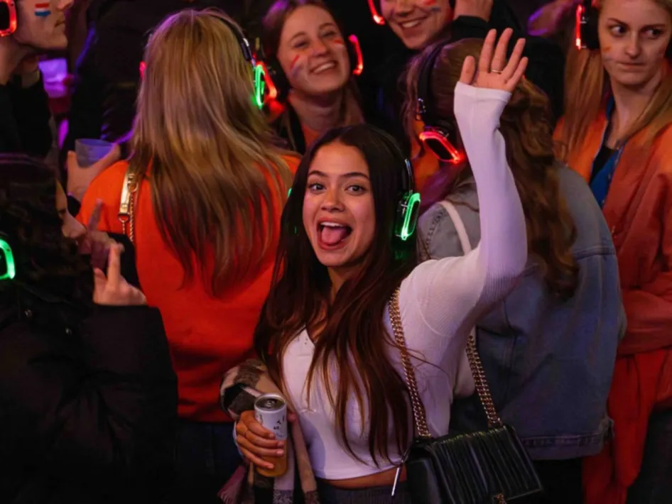 Feestende bezoekers met verlichte koptelefoons tijdens een silent disco, met op de voorgrond een dansende vrouw die haar hand opsteekt.