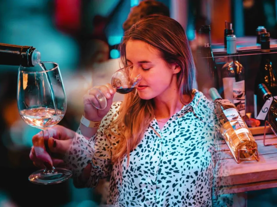Een vrouw ruikt aan een glas rode wijn tijdens een wijnproeverij, terwijl naast haar een glas witte wijn wordt ingeschonken.