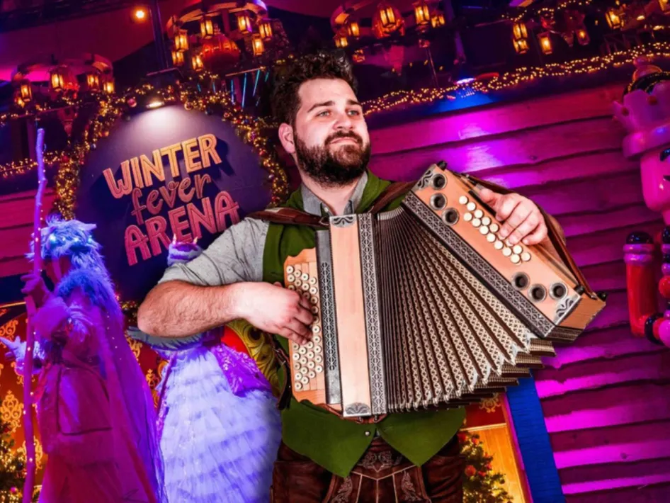 Een muzikant speelt op een trekzak tijdens Trekzak Zondig in de Winter Fever Arena, tussen kleurrijke verlichting en winterse versieringen.