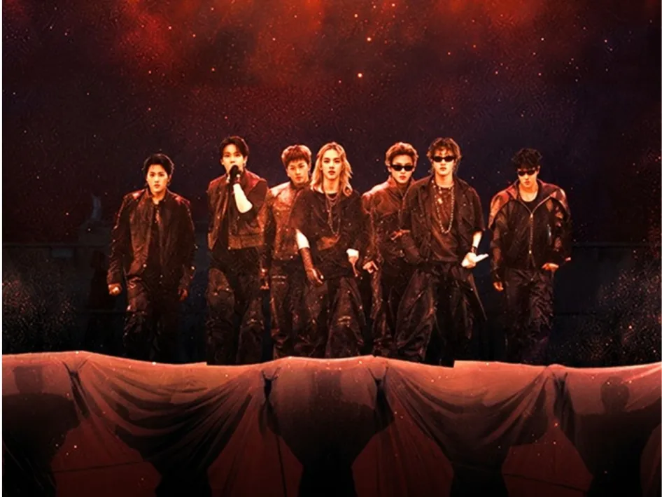 BTS staat in donkere podiumoutfits op een verlicht podium, met rood-oranje spotlights en een dramatische concertsfeer op de achtergrond.