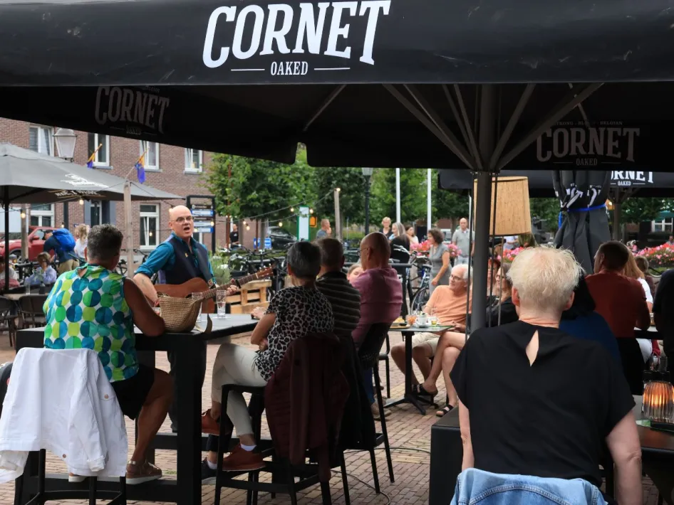 Publiek luistert naar live akoestische muziek tijdens het Akoestisch Festival Beesel op een sfeervol terras in het dorpscentrum.