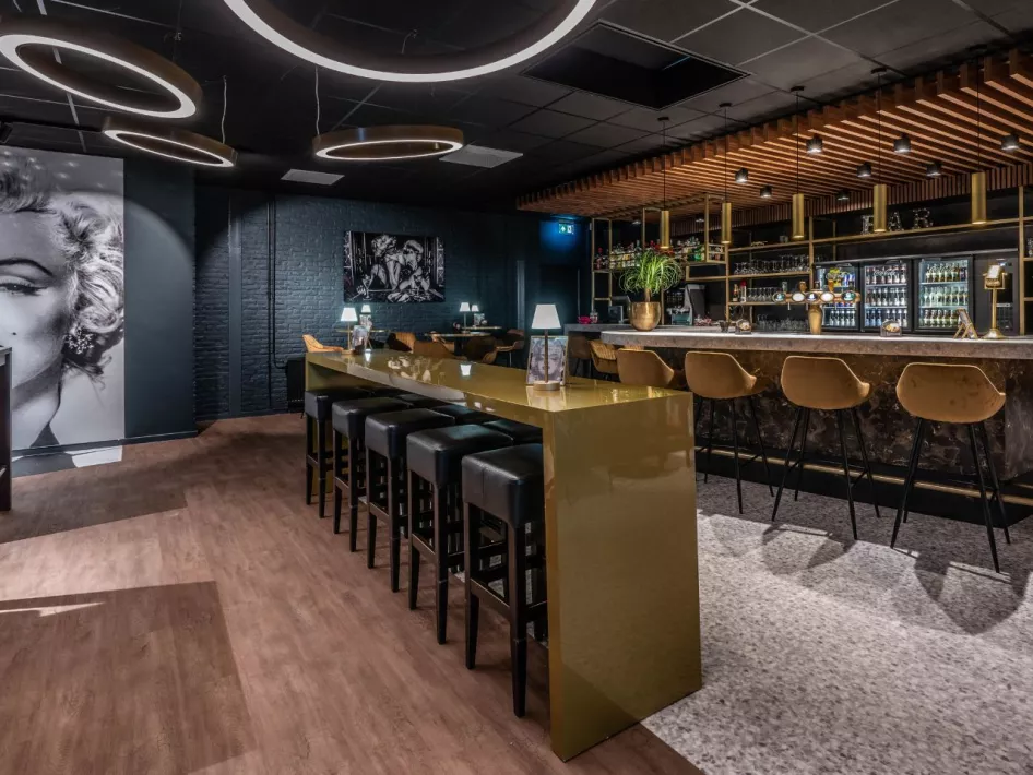 Een stijlvolle bar met gouden accenten en een moderne uitstraling, inclusief een groot portret van Marilyn Monroe aan de muur.