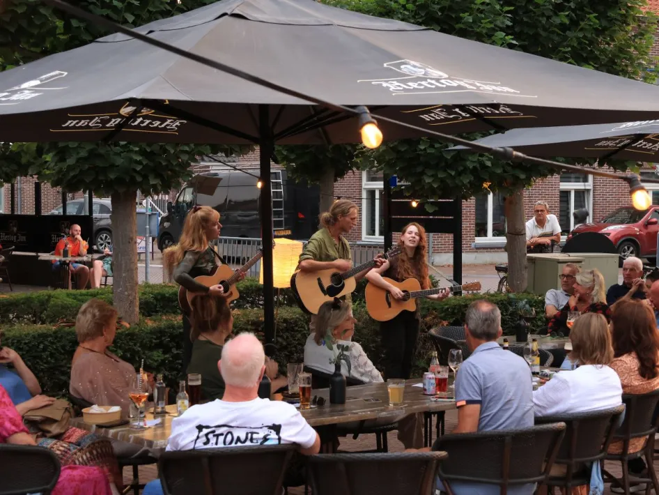 Artiesten spelen live akoestische muziek tijdens het Akoestisch Festival Beesel, omringd door publiek op een gezellig terras in Beesel.