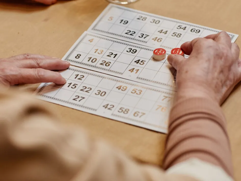 Handen leggen genummerde fiches op kienkaarten tijdens een kienavond.