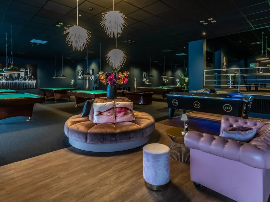 Een ruime en luxe poolhal met meerdere biljarttafels, comfortabele zitplekken en sfeervolle verlichting.