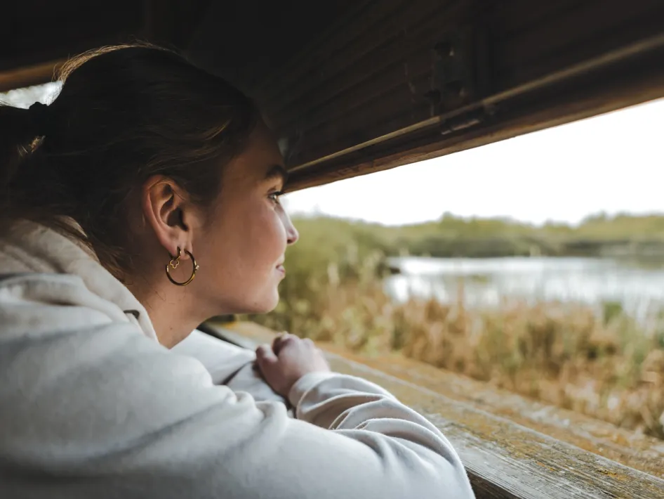 Vrouw kijkt vanuit een vogelkijkhut uit over het water en de natuur van De Groote Peel tijdens de excursie Oog in oog met het Peelwater.