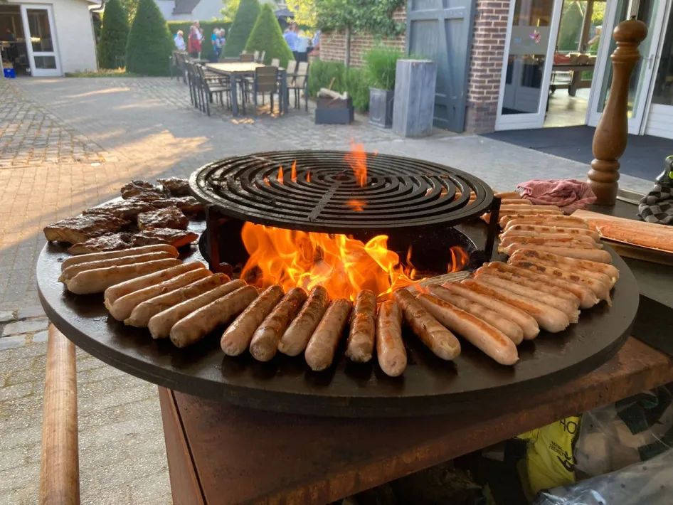 Barbecue bij Oolderhof met vlees op de grill en vuur, onderdeel van een zakelijke bijeenkomst of evenement.