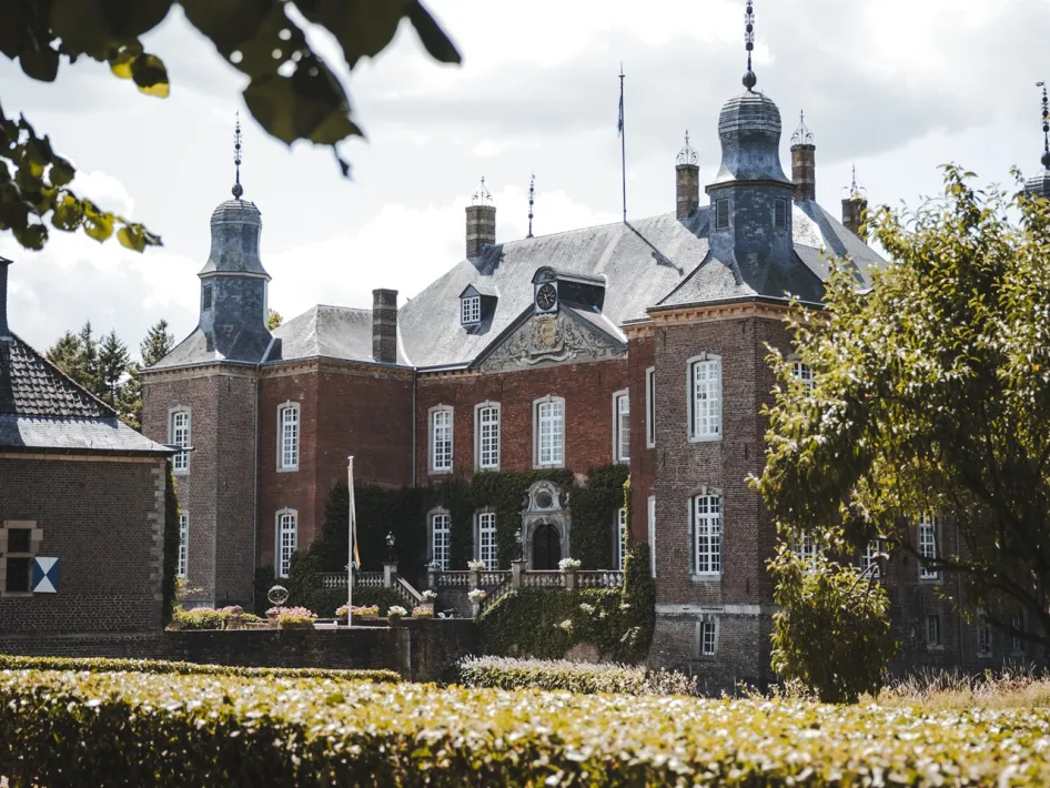 Kasteel Hillenraad in Swalmen, gezien vanaf de tuin met hagen, bomen en de bakstenen gevel op de achtergrond te bezichtigen tijdens de Open Tuinen bij Kasteel Hillenraad.