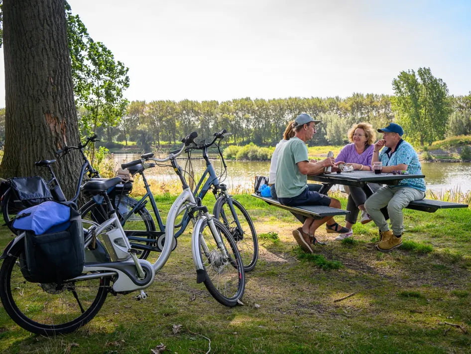 Radfahrer machen eine Pause an einem Picknicktisch an der Maas bei Osen, ihre Fahrräder stehen unter den Bäumen.