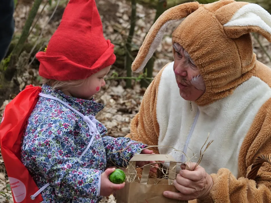 Kind met rood puntmutsje ontmoet paashaas tijdens paasactiviteit in het bos