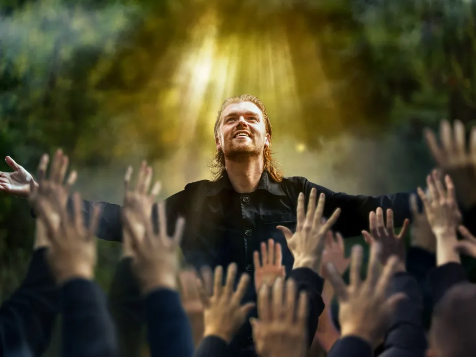 Acteur als Jezus met uitgestrekte armen terwijl handen uit het publiek naar hem reiken tijdens de Passiespelen Tegelen in het openluchttheater.