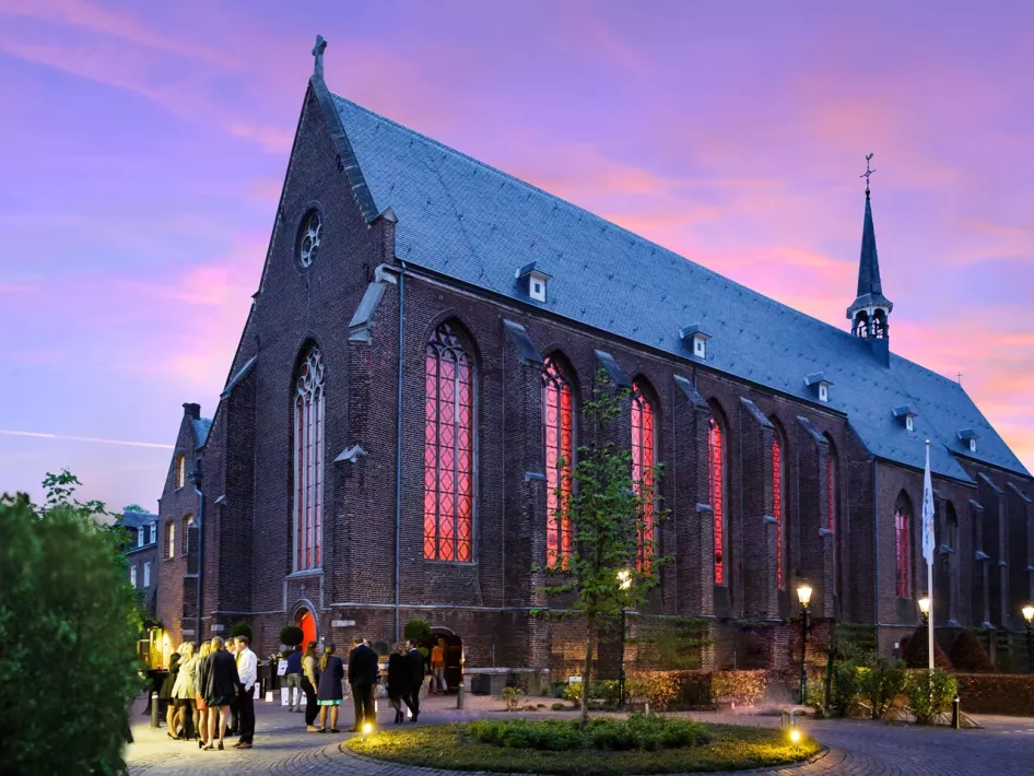 De Paterskerk in Weert tijdens de schemering waar de mensen buiten staan te wachten 