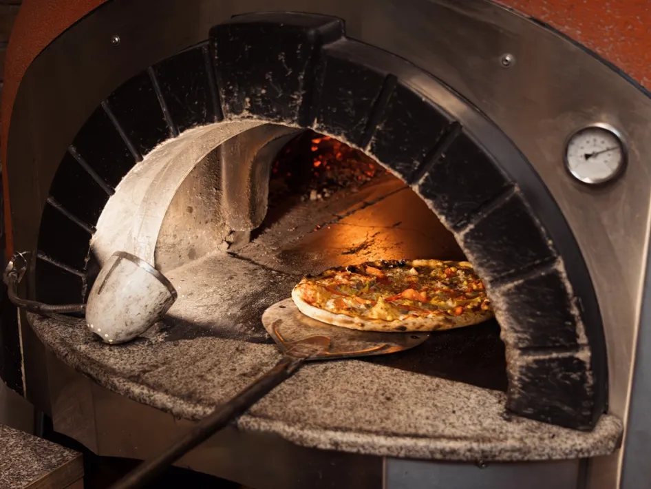 Vers belegde pizza wordt afgebakken in een traditionele steenoven tijdens het pizza bakken in steenoven bij Rijstal Venhof.