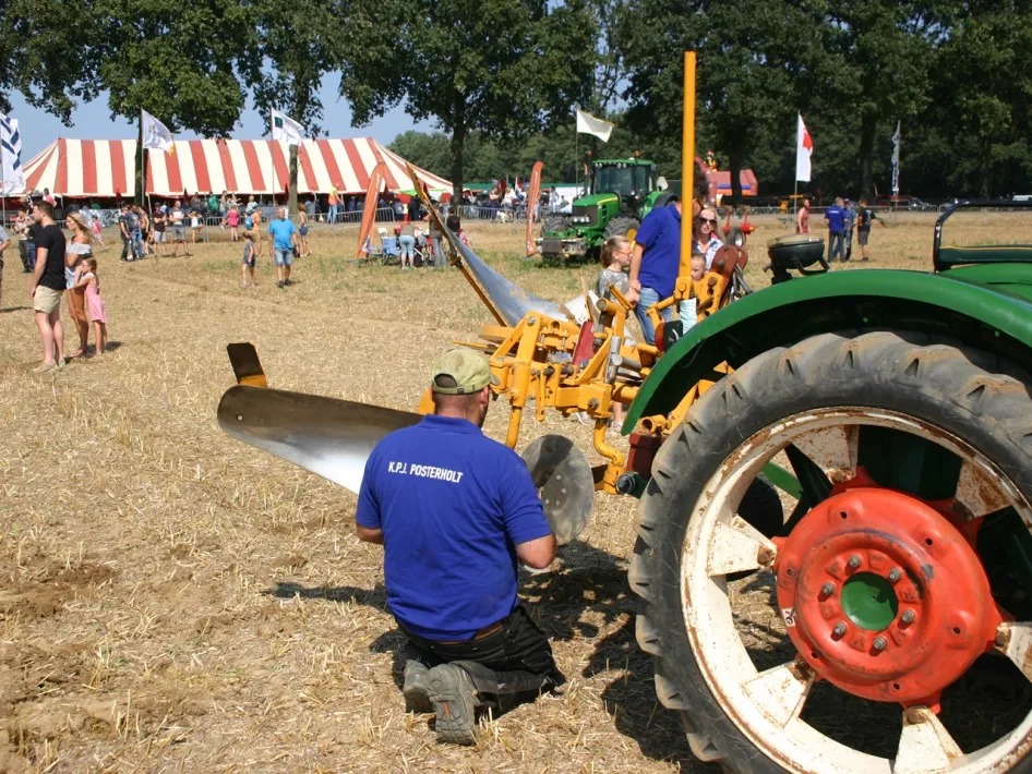 Wedstrijdploeger stelt zijn ploeg af tijdens de Ploegwedstrijd Posterholt, met bezoekers en de feesttent op de achtergrond.