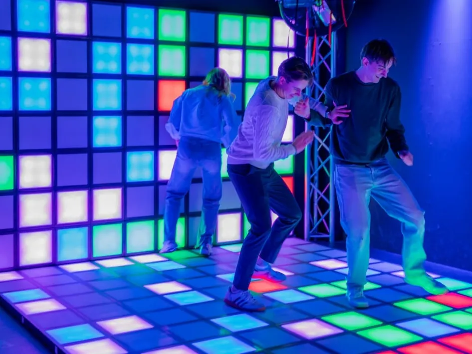Drie jongeren bewegen actief over een kleurrijke vloer met lichtpanelen in de Flash Arena van Poort51.