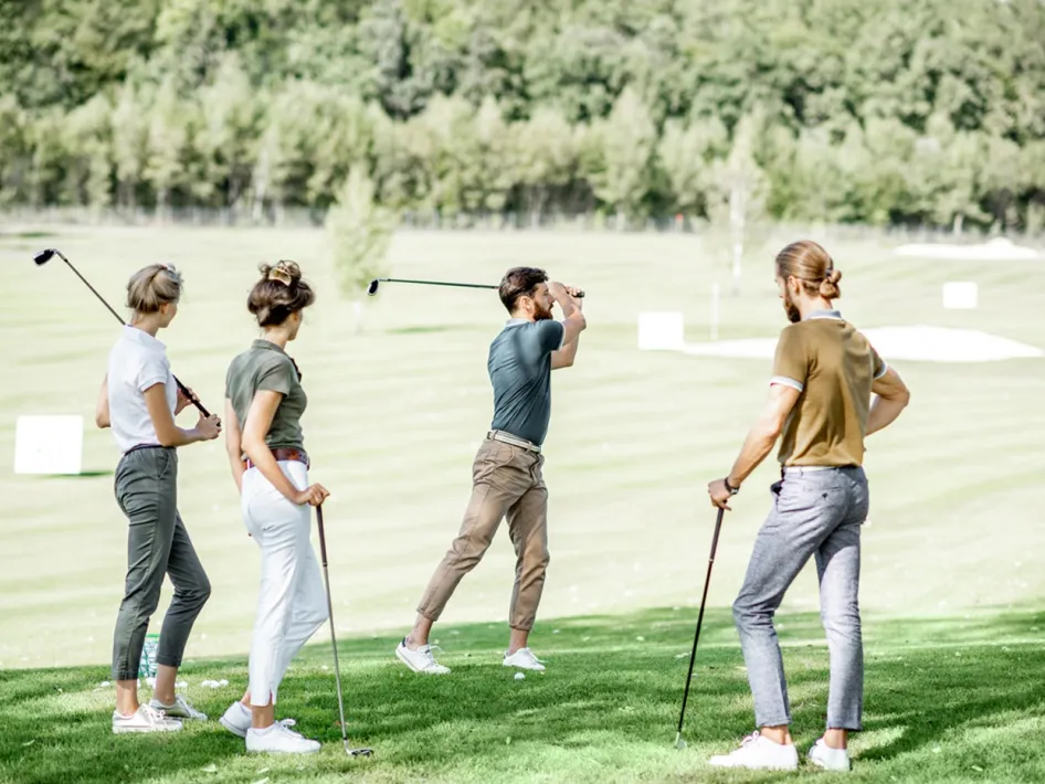 Vier jonge mensen tijdens een golfdag Crossmoor Limburg kijken toe hoe iemand een bal slaat op een zonnige golfbaan.
